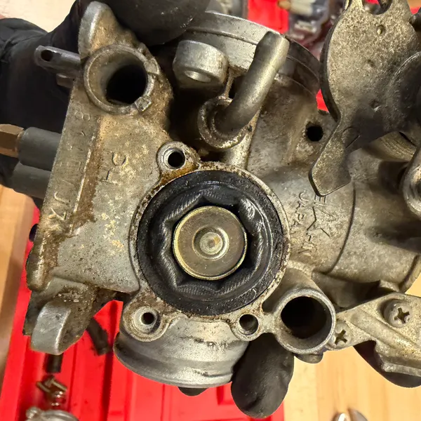 Diaphragm on the side of the carb body, exposed. The rubber is hard and cracking at the edge. Expect to replace these.