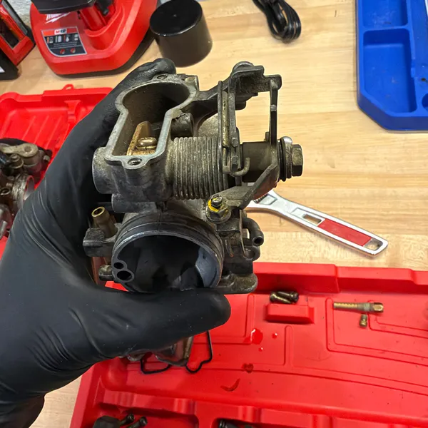 Secondary carb with the bowl off, held up to the light. Float pivot pin and float valve seat visible.