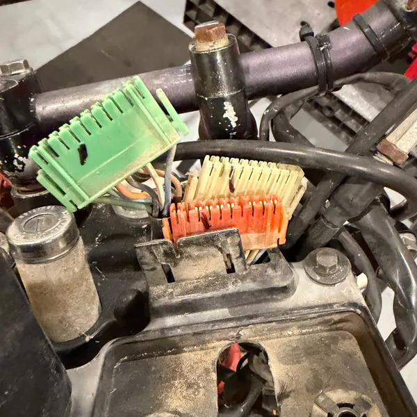 Connectors at the steering head: green six-pin (left) and the cream block (right) with the orange wire bundle. The bracket below is where the headlight shell bolts on.