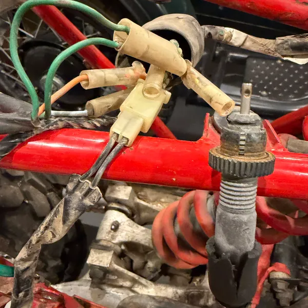 Cable adjuster with its knurled lock nut, hanging free now that the carbs are off, next to the bullet connectors by the shock. The cream connector block and green wires are the rear harness branch.