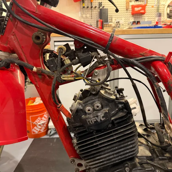 Engine in the frame with the tank, airbox, carbs and header all off. RFVC head, left side. Front fender still on at this point.