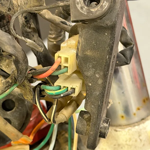 Horn bracket bolted to the lower triple clamp, connectors behind it. Green and orange wires.