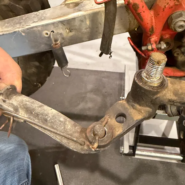 Brake pedal off its pivot. Return spring still hanging on the frame, pivot stud exposed with its washer. The clevis at the end is where the rod attaches.